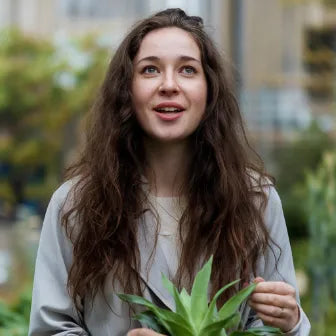 Mujer sonriente con planta suculenta en jardín urbano, ideal para mascotas y hogar