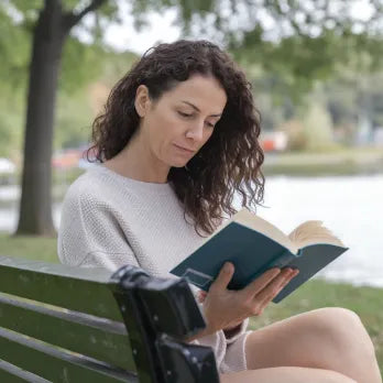 Mujer leyendo libro en banco de parque, disfrutando de momento tranquilo al aire libre