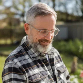 Hombre sonriente con barba y gafas en jardín, disfrutando del aire libre con su mascota