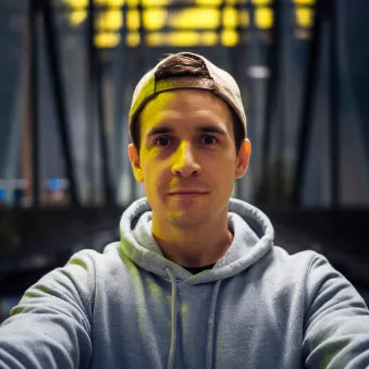Hombre joven con gorra y sudadera gris tomando selfie en entorno urbano nocturno