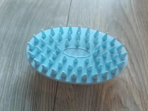 Cepillo masajeador para mascotas con puntas suaves en azul claro sobre piso de madera
