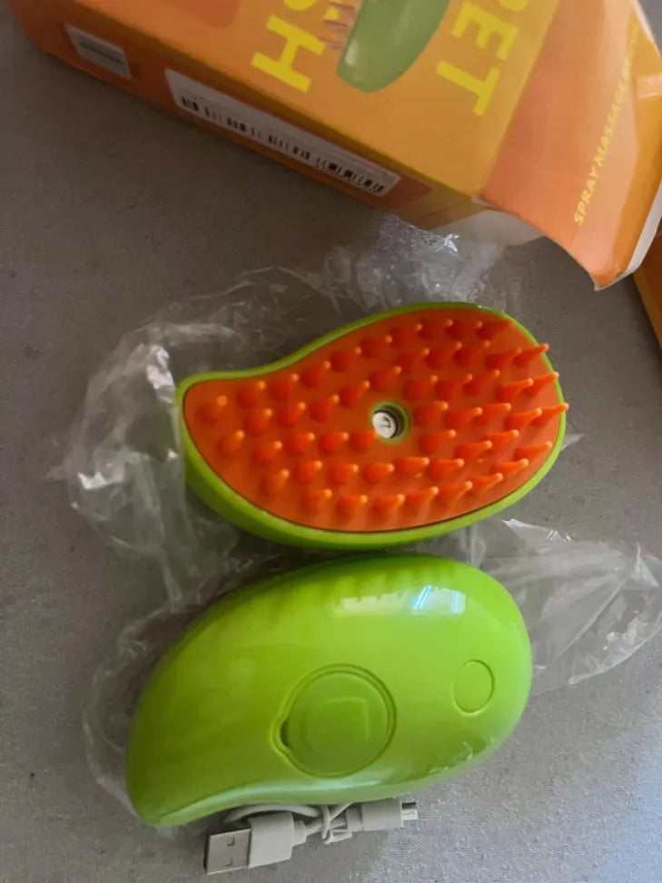 Cepillo masajeador para mascotas con vibración y spray, color verde y naranja, ideal para el cuidado de perros y gatos.