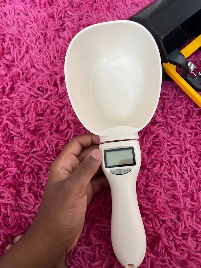 Cuchara medidora digital para comida de mascotas sobre alfombra rosa